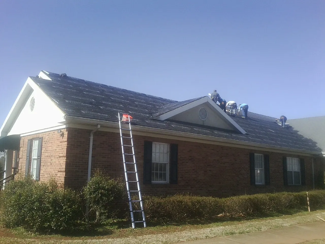 Crew tearing shingles off a brick ranch roof with a ladder set — Emergency Roof Repair work by our crew in Nellysford