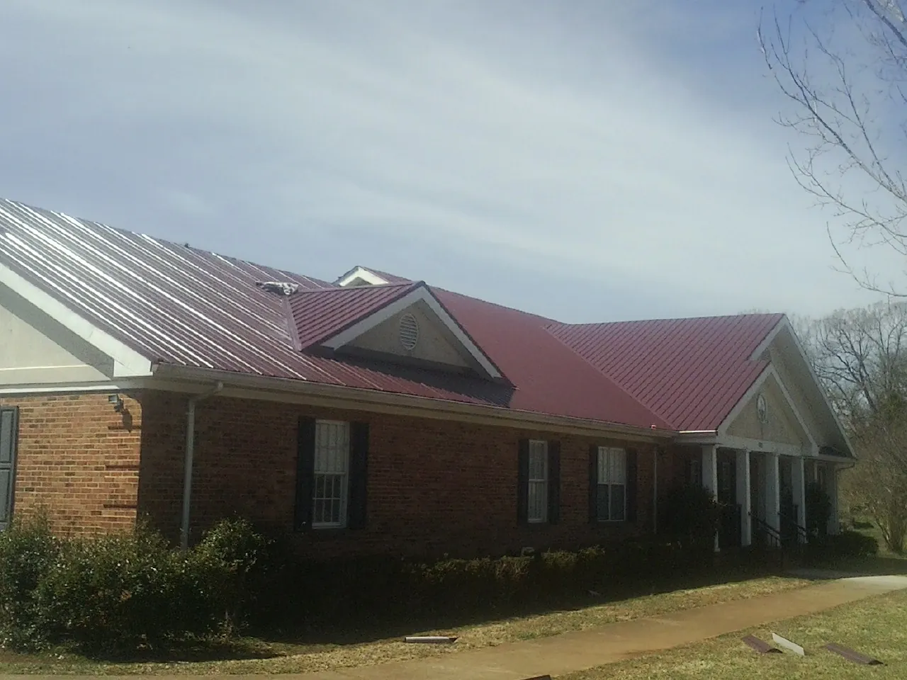 Red metal roof with gabled entries on a long brick building, from a Hail Damage Roof Repair job in Nellysford
