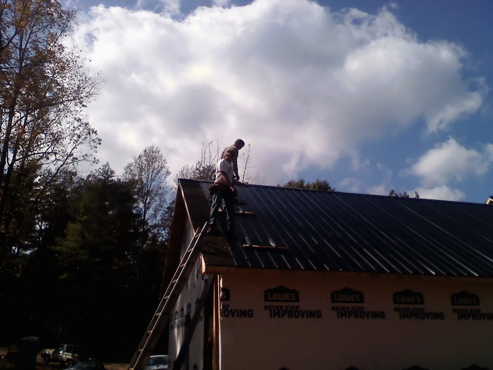 Roofer fastening dark metal panels high against a cloudy sky, from a Roof Inspection job in Nellysford