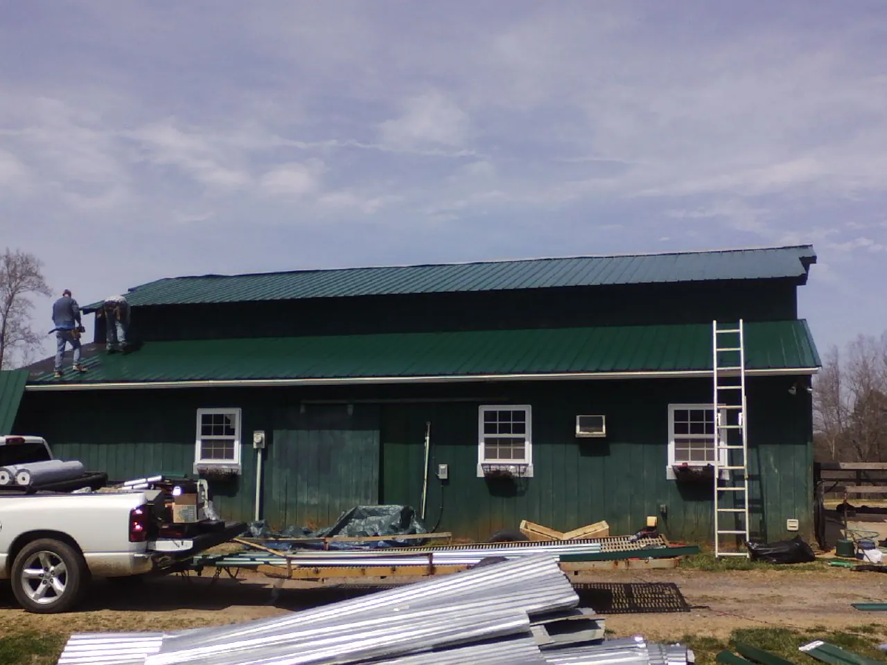 Crew installing green metal roofing on a large green barn in Nellysford