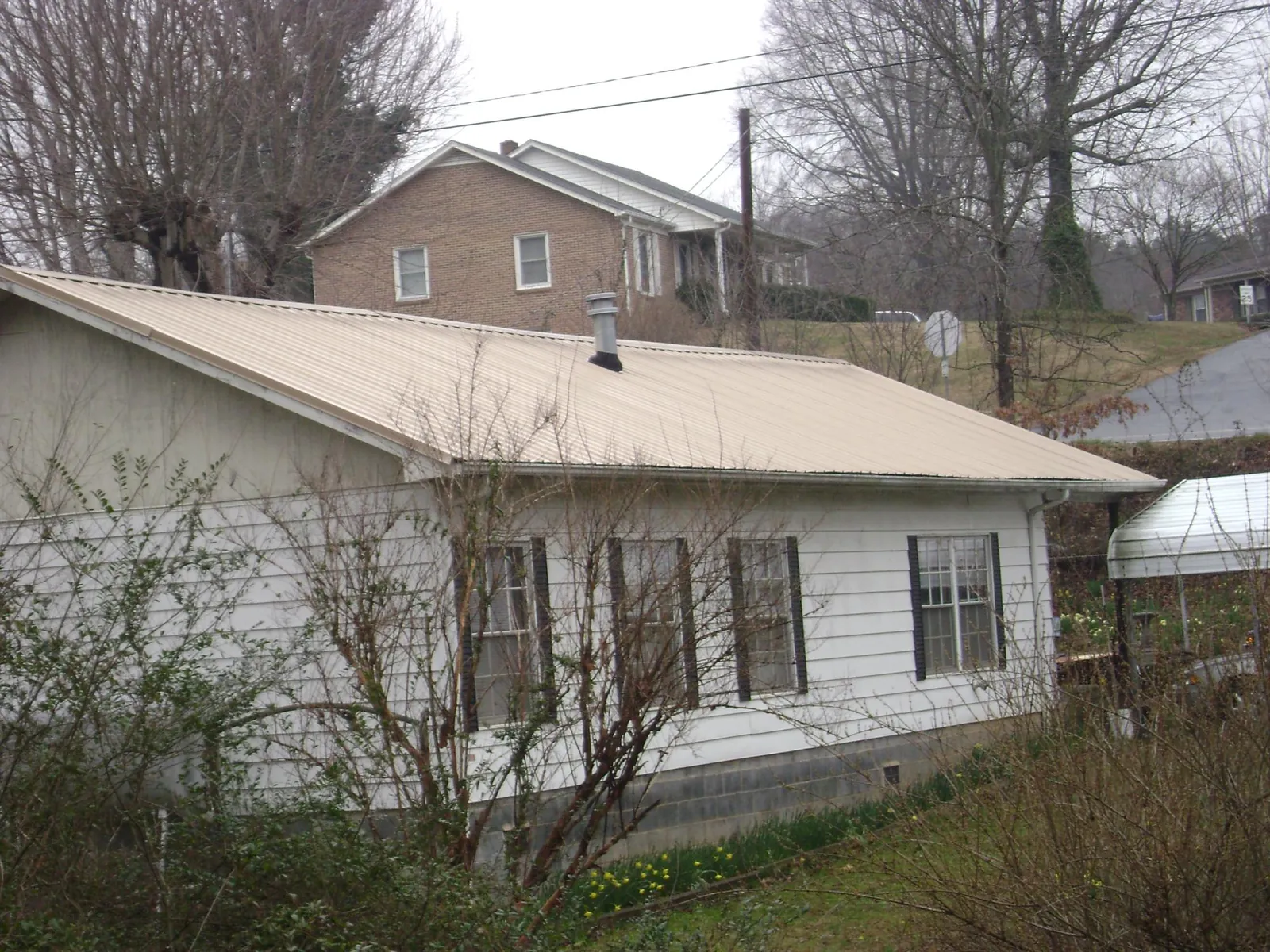 Tan metal roof on a white sided house set into a hillside — Commercial Roofing by Roofing Brothers in Nellysford