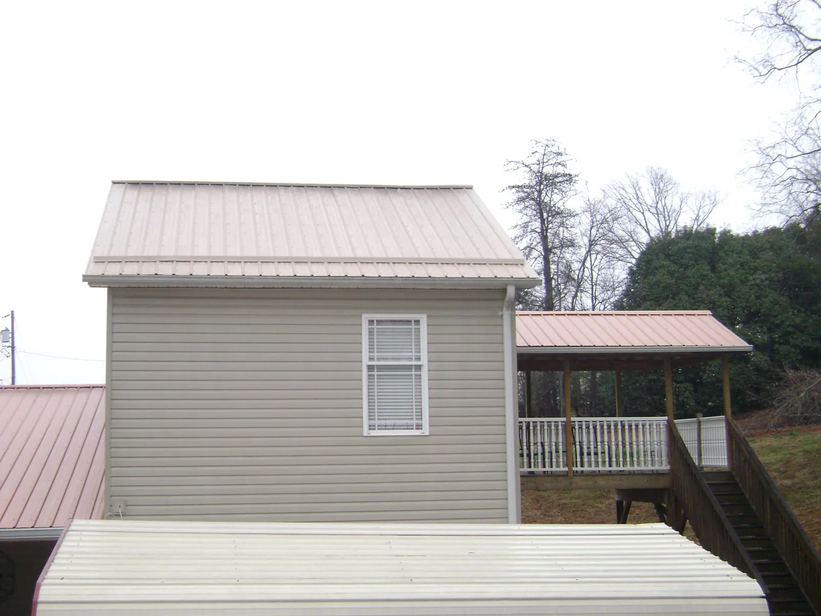 Tan metal roofs on a two story addition and attached porch, from a Roof Replacement job in Nellysford